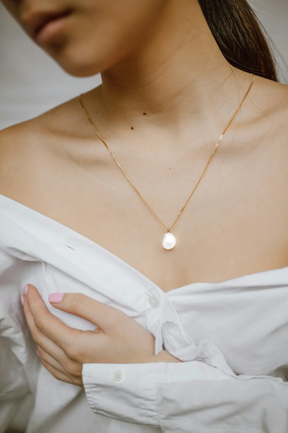 A gold pendant necklace worn with a white shirt